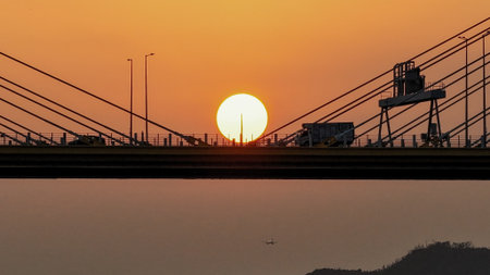 Bridge silhouettes frame a glowing sunset over calm water, w