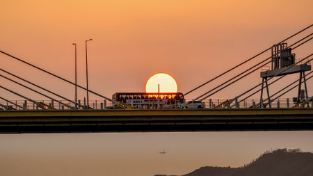 A dramatic sunset casts warm orange light over a city bridgeの写真素材