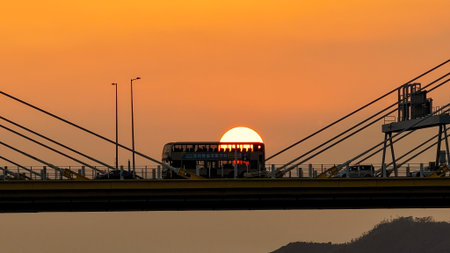 A dramatic sunset casts warm orange light over a city bridgeの写真素材