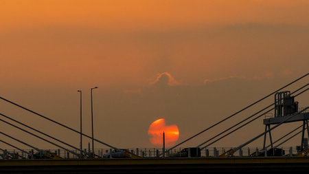 A dramatic sunset casts warm orange light over a city bridge