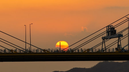 A dramatic sunset casts warm orange light over a city bridgeの写真素材