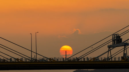 A dramatic sunset casts warm orange light over a city bridgeの写真素材
