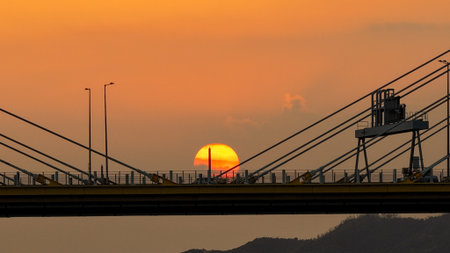 A dramatic sunset casts warm orange light over a city bridgeの写真素材