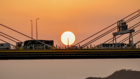 Bridge silhouettes frame a glowing sunset over calm water, wの写真素材