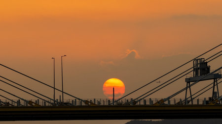 A dramatic sunset casts warm orange light over a city bridgeの写真素材