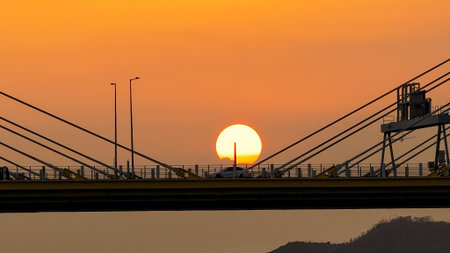 A dramatic sunset casts warm orange light over a city bridgeの写真素材