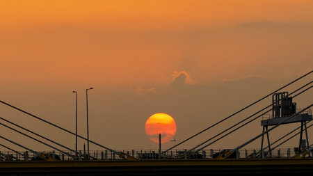 A dramatic sunset casts warm orange light over a city bridgeの写真素材