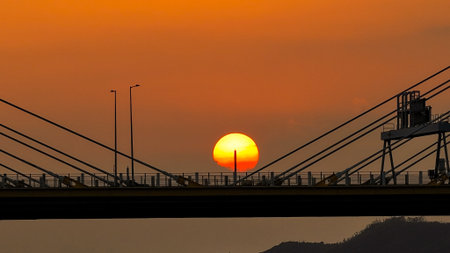 A dramatic sunset casts warm orange light over a city bridgeの写真素材