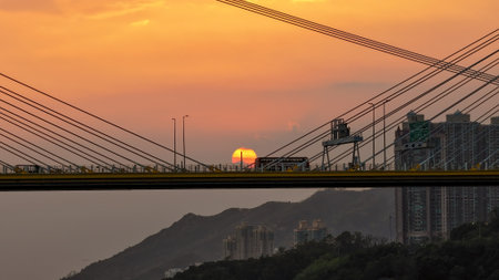 A dramatic sunset casts warm orange light over a city bridgeの写真素材