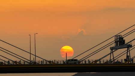 A dramatic sunset casts warm orange light over a city bridgeの写真素材