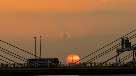 A dramatic sunset casts warm orange light over a city bridgeの写真素材