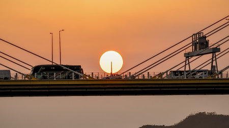 Bridge silhouettes frame a glowing sunset over calm water, w