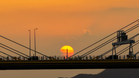 A dramatic sunset casts warm orange light over a city bridgeの写真素材
