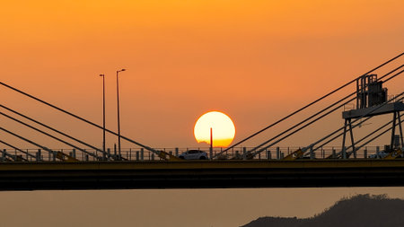 A dramatic sunset casts warm orange light over a city bridgeの写真素材