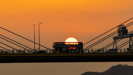 A dramatic sunset casts warm orange light over a city bridgeの写真素材