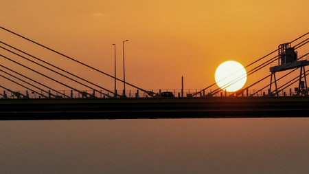 A dramatic sunset casts warm orange light over a city bridgeの写真素材