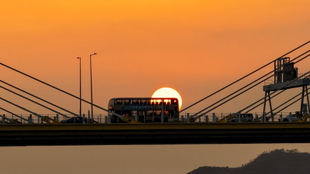 A dramatic sunset casts warm orange light over a city bridgeの写真素材