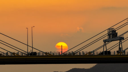 A dramatic sunset casts warm orange light over a city bridgeの写真素材