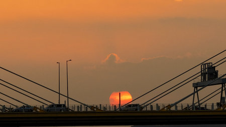 A dramatic sunset casts warm orange light over a city bridgeの写真素材