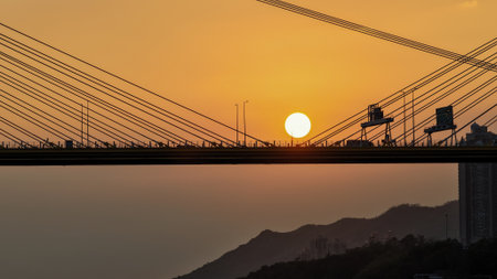 A dramatic sunset casts warm orange light over a city bridgeの写真素材