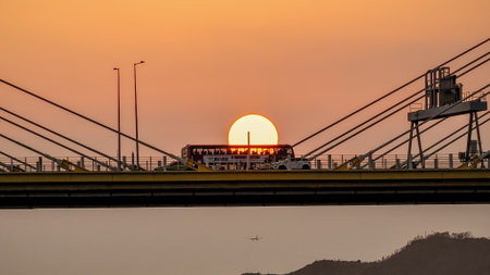 A dramatic sunset casts warm orange light over a city bridgeの写真素材