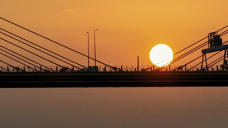 A dramatic sunset casts warm orange light over a city bridgeの写真素材