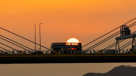 A dramatic sunset casts warm orange light over a city bridgeの写真素材