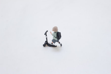 A tiny plastic figure rides a black kick scooter, wearing a backpackの写真素材