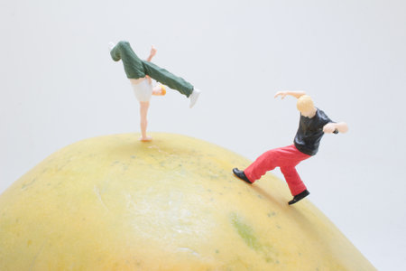 large yellow mango sits on a white surface while two tiny figurinesの写真素材