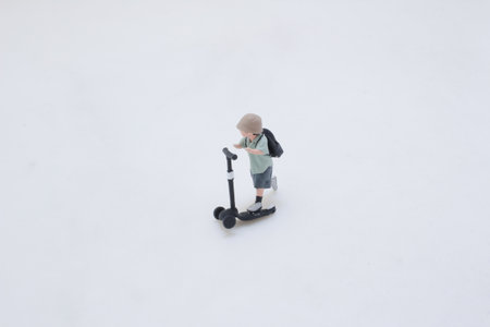 A tiny plastic figure rides a black kick scooter, wearing a backpackの写真素材