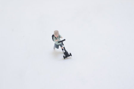 A tiny plastic figure rides a black kick scooter, wearing a backpackの写真素材