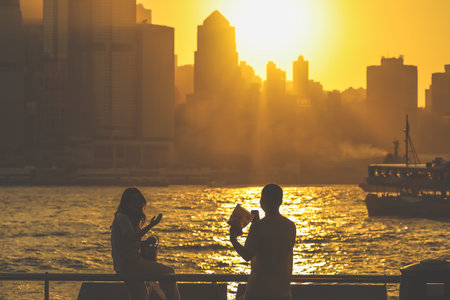 Two silhouetted figures by a railing overlook a golden sunset Nov 16 2025のeditorial素材
