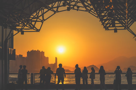 Silhouetted figures line a waterfront promenade as the sun sinks behind Nov 16 2025のeditorial素材
