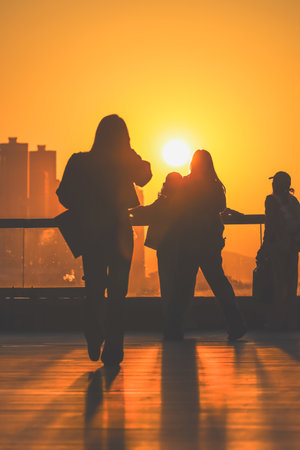 figures stand by a glass railing as a brilliant orange sunset Nov 16 2025のeditorial素材