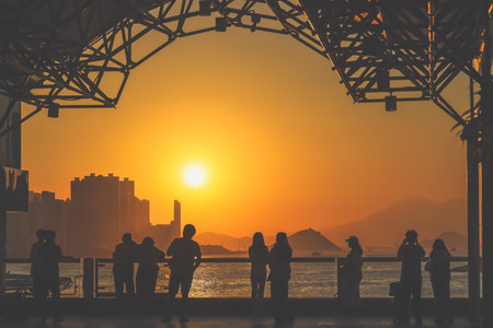 Silhouetted figures line a waterfront promenade as the sun sinks behind Nov 16 2025のeditorial素材