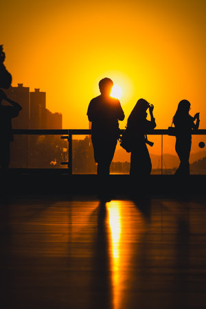 figures stand by a glass railing as a brilliant orange sunset Nov 16 2025のeditorial素材