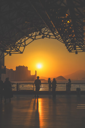 Silhouetted figures line a waterfront promenade as the sun sinks behind Nov 16 2025のeditorial素材