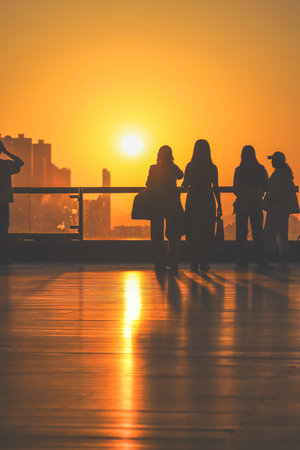 figures stand by a glass railing as a brilliant orange sunset Nov 16 2025のeditorial素材