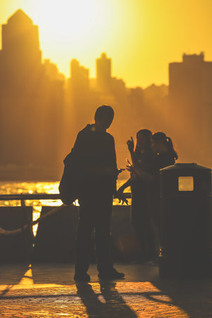 Silhouettes of visitors stand against a golden sunset as a dense city skyline Nov 16 2025のeditorial素材