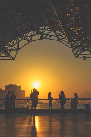 Silhouetted figures line a waterfront promenade as the sun sinks behind Nov 16 2025のeditorial素材