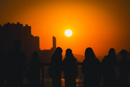 figures stand by a glass railing as a brilliant orange sunset Nov 16 2025のeditorial素材