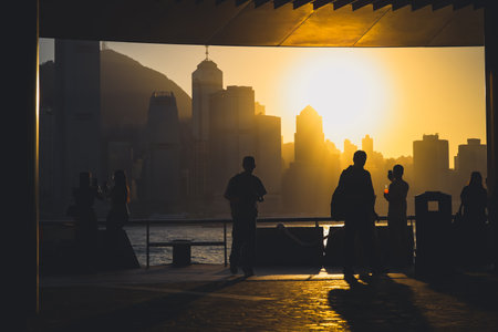 Silhouetted figures stand along a waterfront promenade as a warm sunset Nov 16 2025のeditorial素材