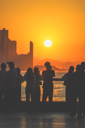 Silhouetted group stands on a sunlit balcony as the city skyline glows Nov 16 2025のeditorial素材