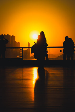 figures stand by a glass railing as a brilliant orange sunset Nov 16 2025のeditorial素材
