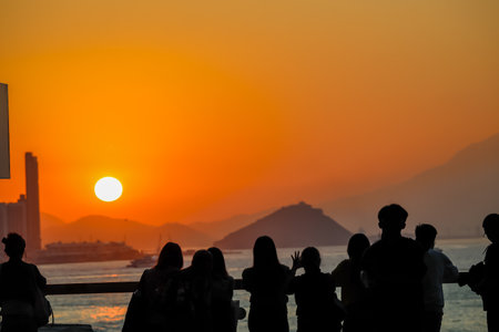 figures stand by a glass railing as a brilliant orange sunset Nov 16 2025のeditorial素材
