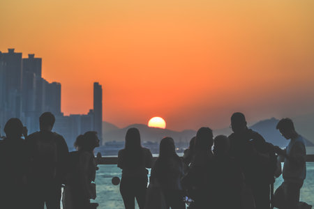 Silhouetted group stands on a sunlit balcony as the city skyline glows Nov 16 2025のeditorial素材