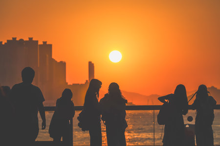 figures stand by a glass railing as a brilliant orange sunset Nov 16 2025のeditorial素材