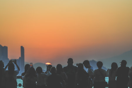 Silhouetted group stands on a sunlit balcony as the city skyline glows Nov 16 2025のeditorial素材