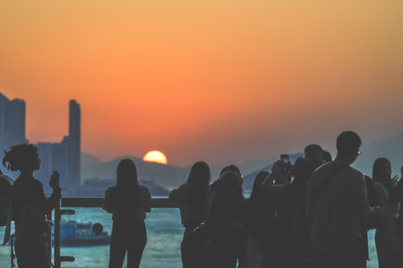 Silhouetted group stands on a sunlit balcony as the city skyline glows Nov 16 2025のeditorial素材