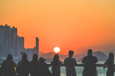 Silhouetted group stands on a sunlit balcony as the city skyline glows Nov 16 2025のeditorial素材